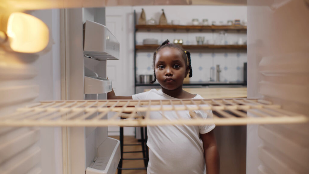 Child looking into an empty refrigerator, symbolizing food insecurity.